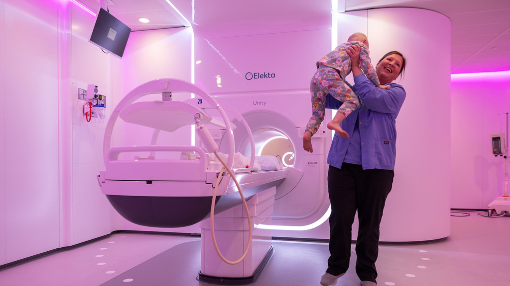 A woman holding a child and laughing while standing beside an MRI machine