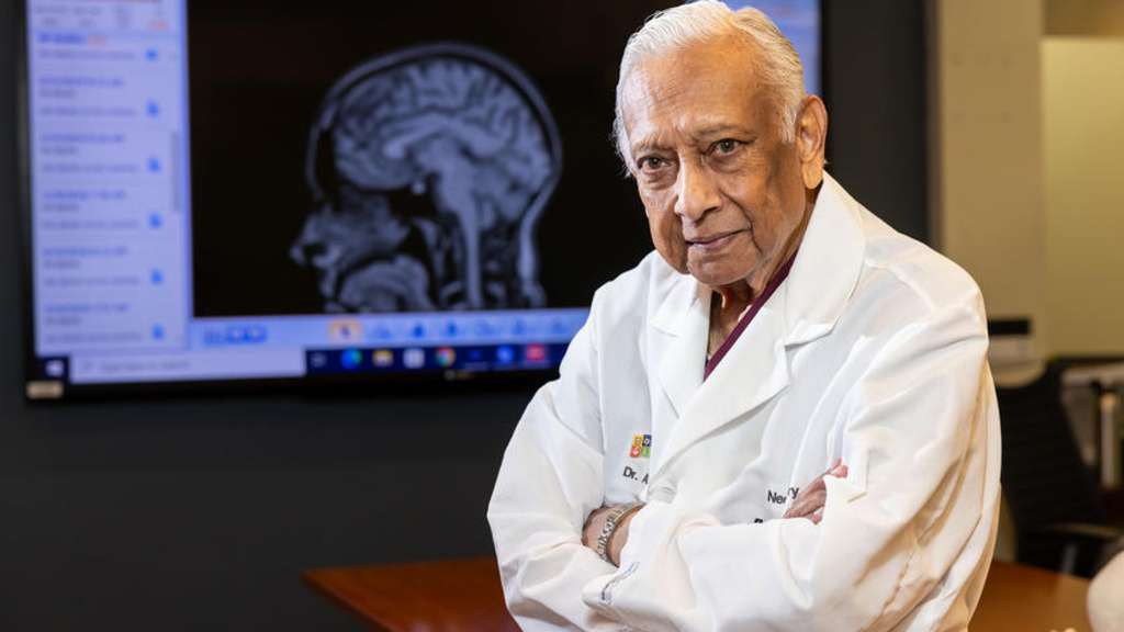 A doctor leaning on a table while a brain scan is shown in the background