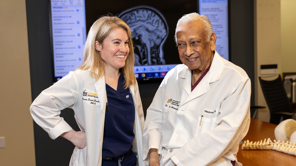 Two doctors smiling for a photo in front of a screen