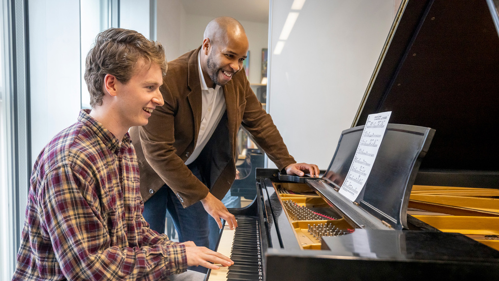 two men sitting behind a piano testing a song