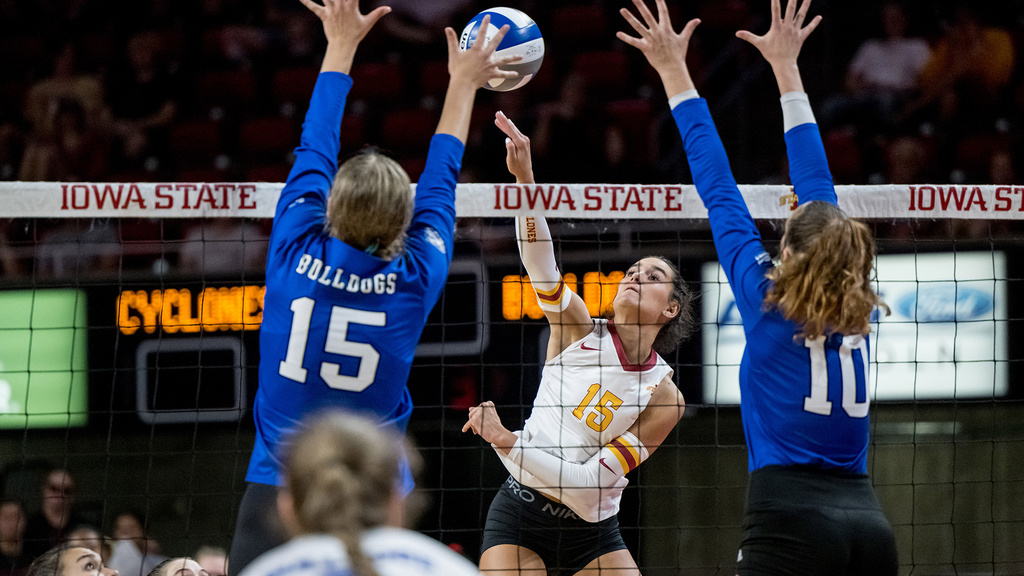 a volleyball player leaps to spike the ball while two defenders jump in an attempt to block