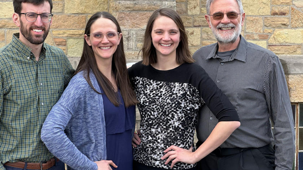 A family of four standing in front of a limestone wall smiling