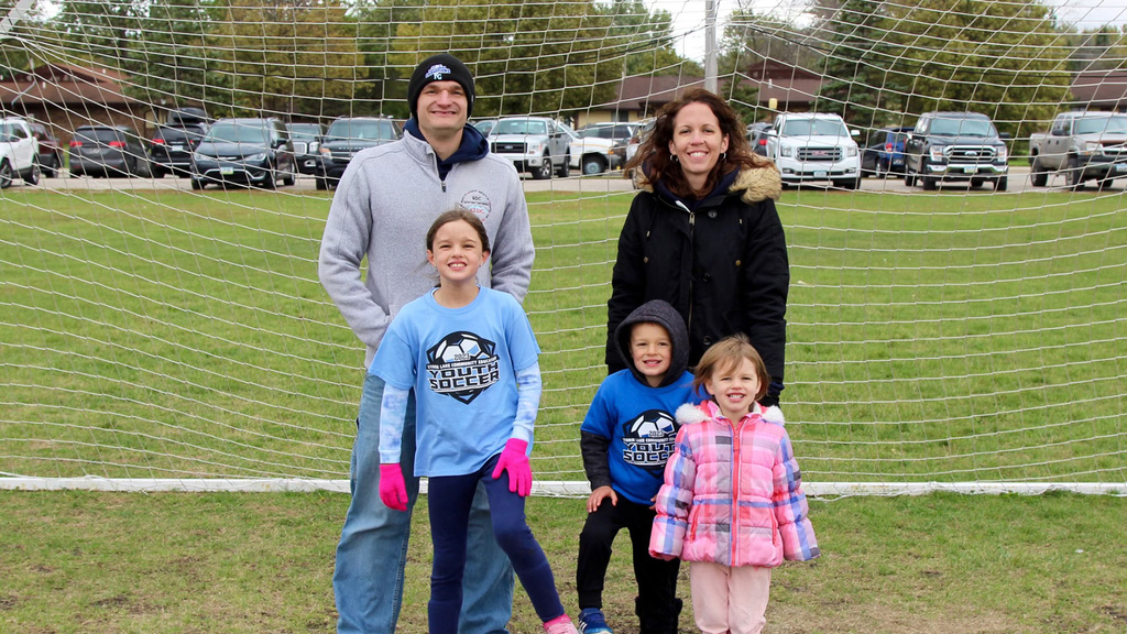 A family of five standing in font of a soccer net