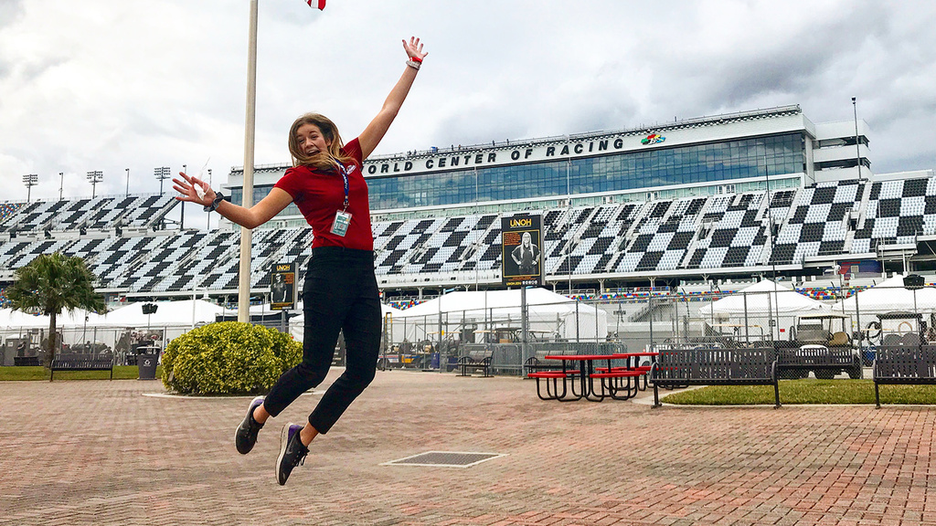 a woman leaps in the air in celebration outside of a racing venue