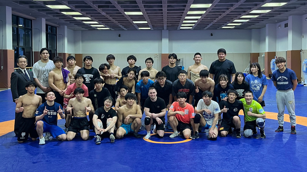 A group of wrestlers standing on a mat smiling