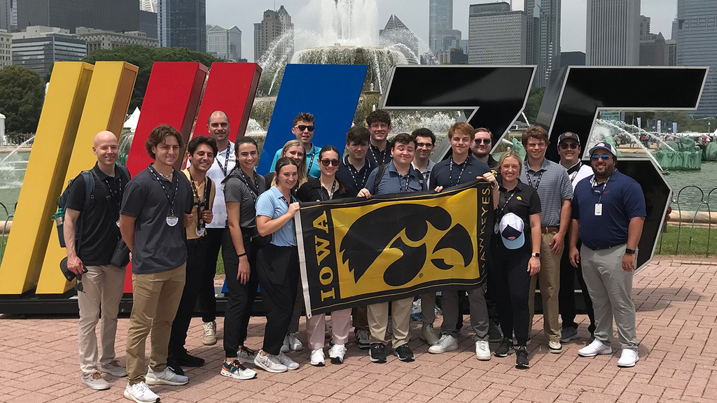 a group of people standing before a NASCAR display, holding a University of Iowa flag