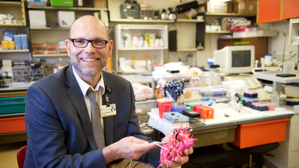 A man sitting in a lab holding a model of a heart