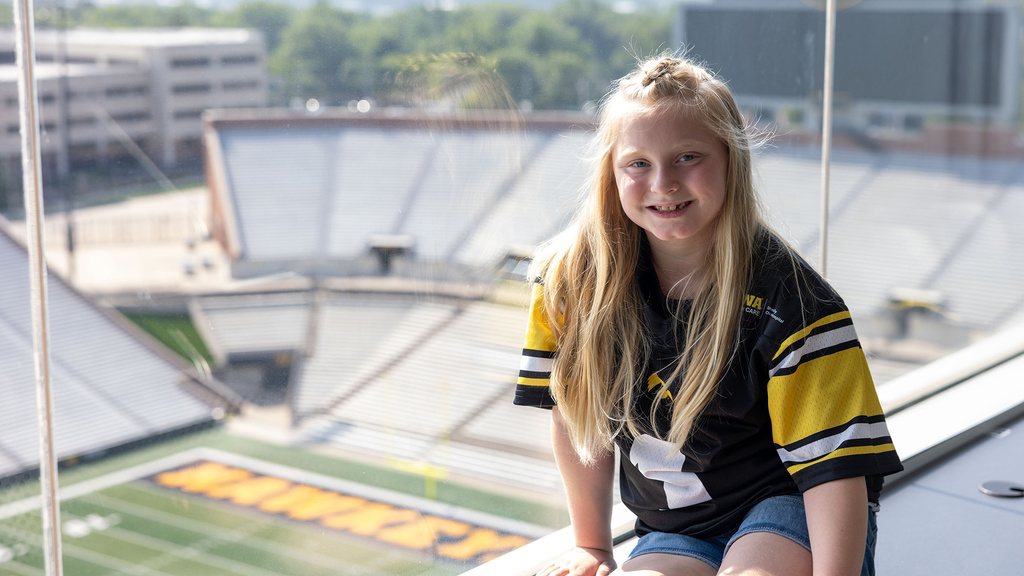 A young girl sitting on a window sill looking over a football field