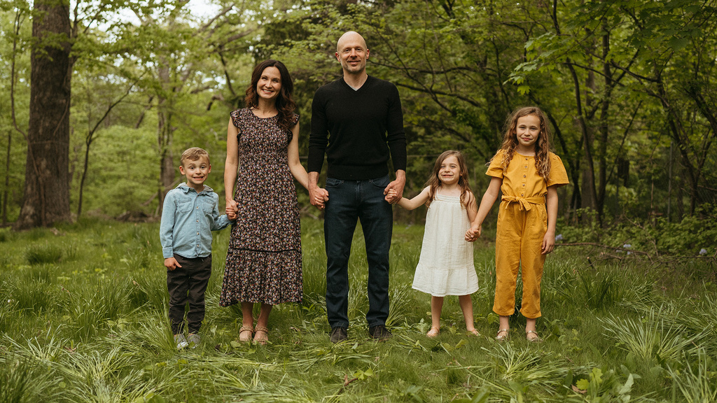a family of five (mom, dad, three kids) stand outdoors for a portrait
