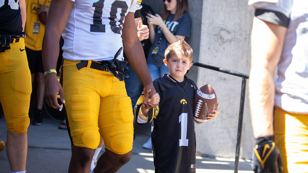 a young boy walking with a football player while holding a football