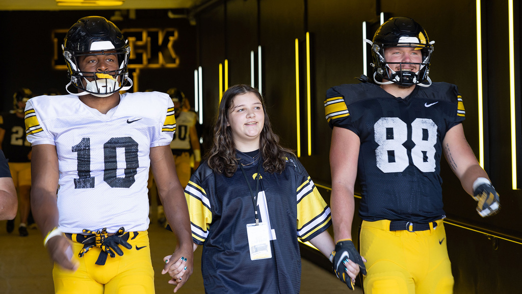 A girl standing with two football players walking through a tunnel