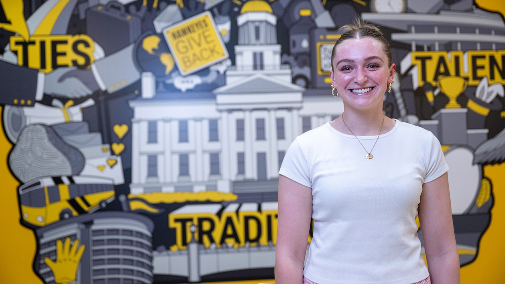University of Iowa student Lillian Wischmeyer standing in front of an Iowa mural