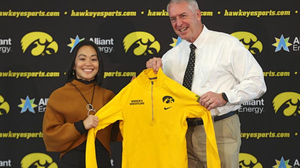 University of Iowa women's wrestling coach Clarissa Chun with athletics director Gary Barta, holding up a gold pullover with a women's wrestling wordmark