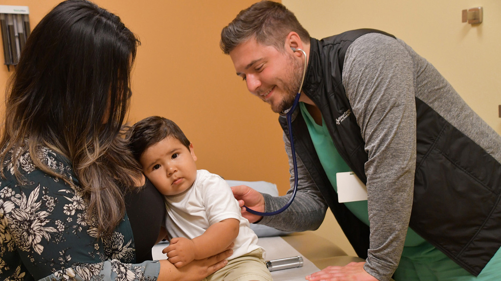 a doctor examines a young boy who is being held by a parent