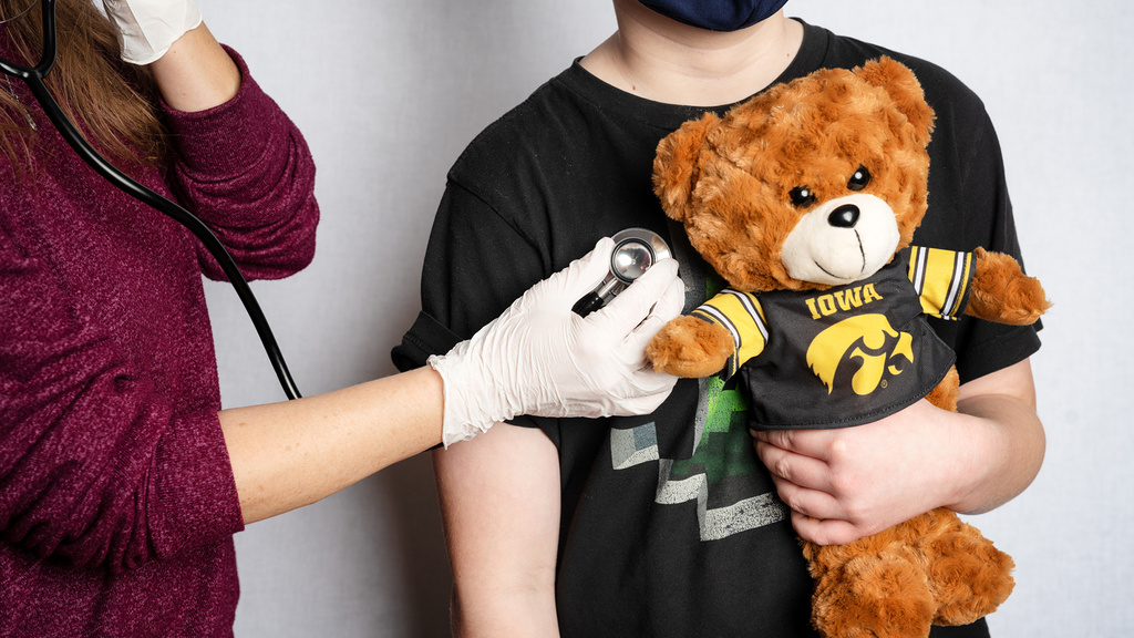 A child holding a teddy bear while their breathing is listened to