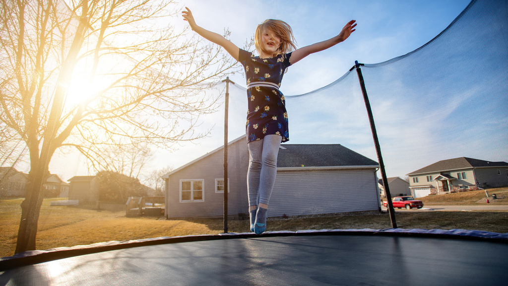 a young girl jumping on a trampoline outdoors in her neighborhood