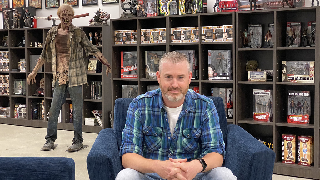 A man sitting in a room with a wall of "Walking Dead" merchandise