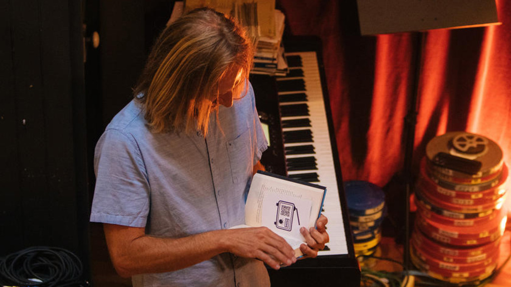 JC Geiger standing before a keyboard, holding a book