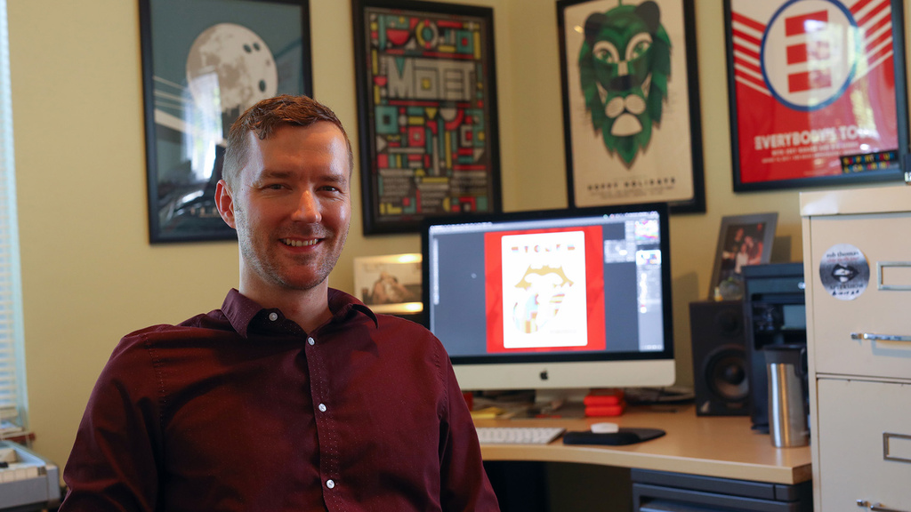 a man sitting in his office, the walls of which are adorned with posters he designed