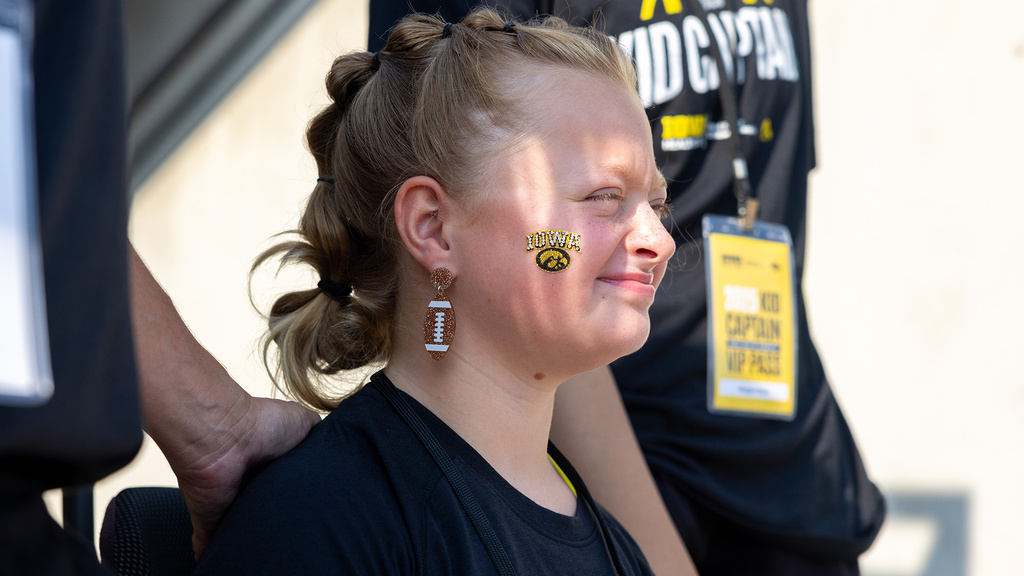 a young girl with a Hawkeye decal on her cheek looks toward the football field at Kinnick Stadium