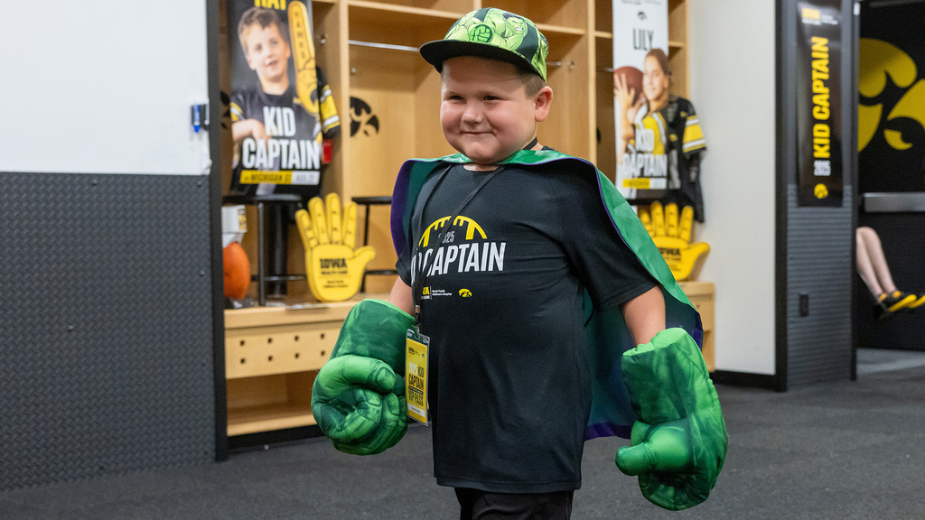 Kid Captain Micah Norby walking through the Kinnick locker room wearing Hulk hands and a cape