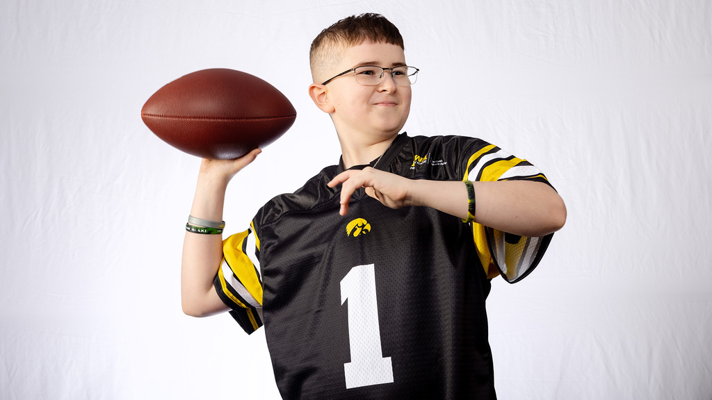 a young boy wearing an Iowa Hawkeyes jersey brings his arm back to throw a football