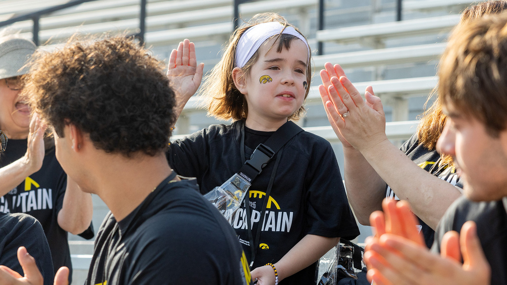 a young girl wearing an iowa hawkeyes jersey raises her hand to deliver a high-five to a nearby friend or family member