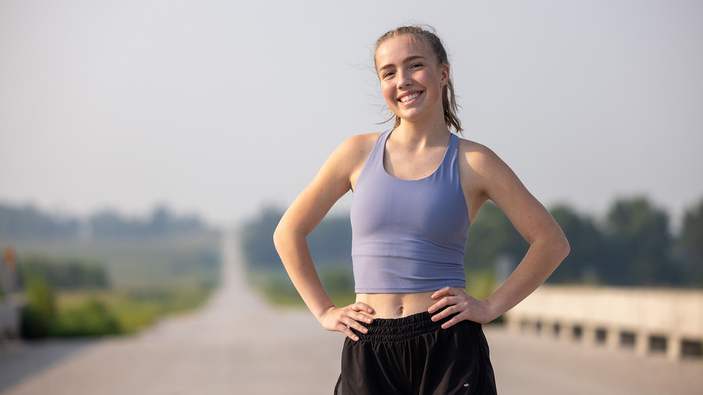 a young woman wearing running apparel stands on a rural road 