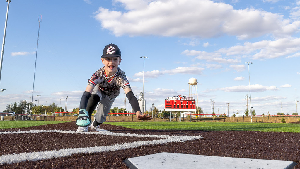 a boy sliding headfirst at home plate on a baseball field