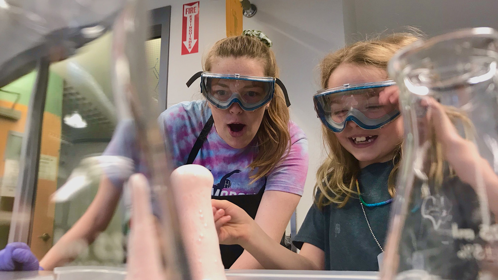 an older girl conducts a science experiment with a younger student