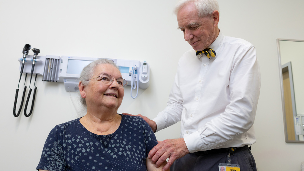 a health care professional examines a woman's shoulder while she sits in a medical facility room