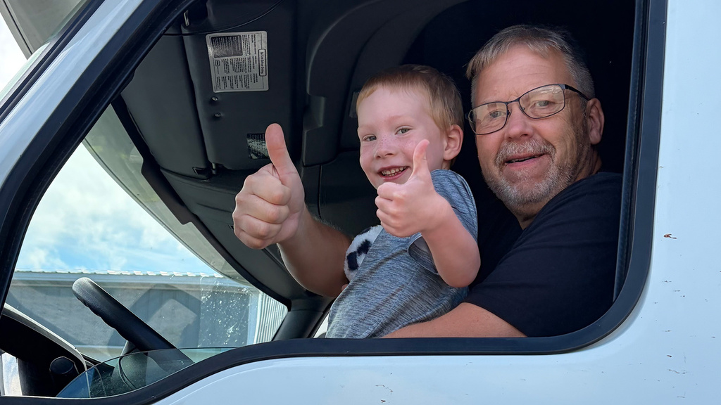 a man and his grandson give a thumbs-up signal through the open window of a vehicle