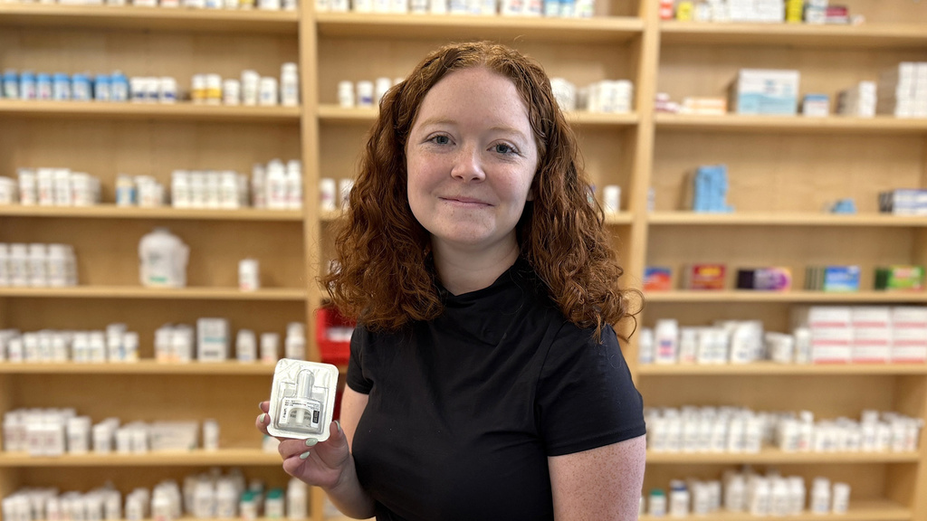 a pharmacy student holding naloxone, standing before shelves with medications