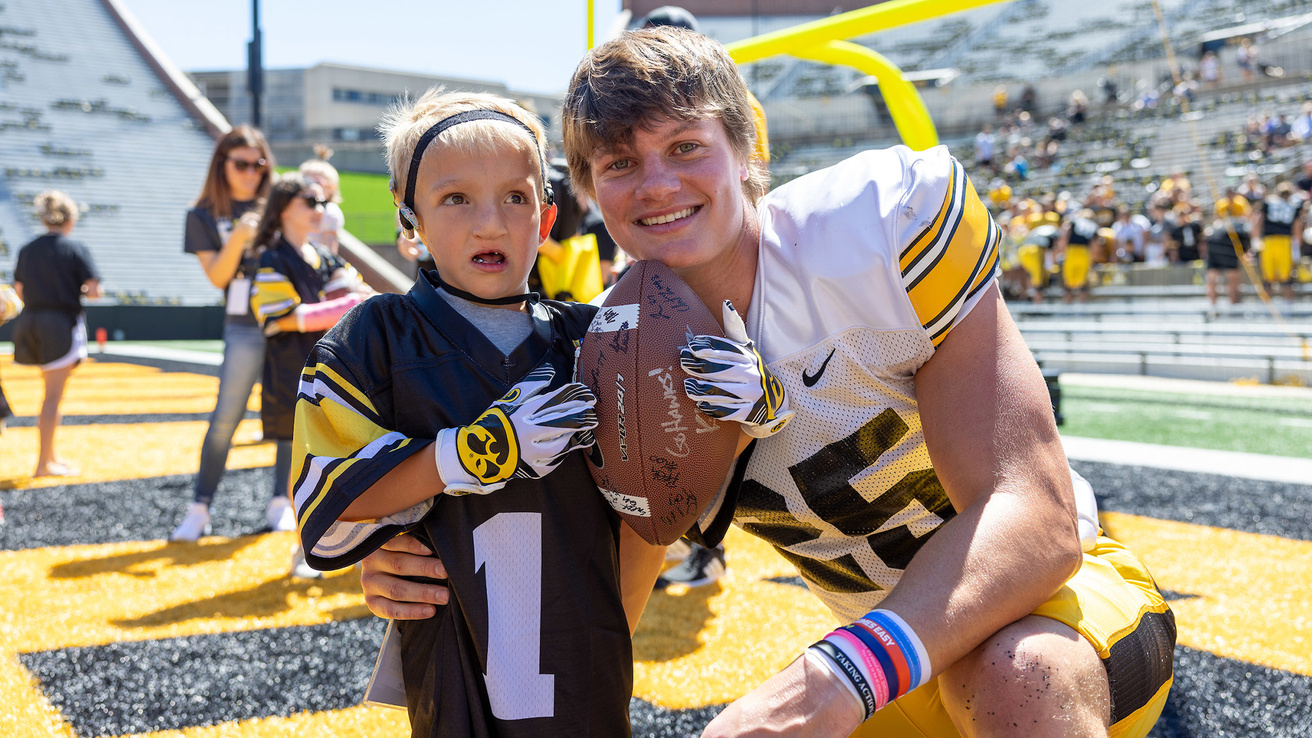 A football player kneeling down and smiling with a young boy