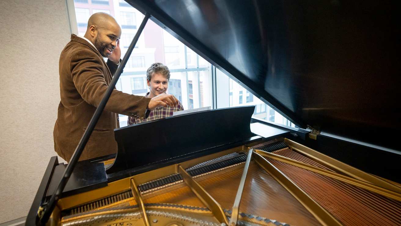 two men sitting at a piano and practicing