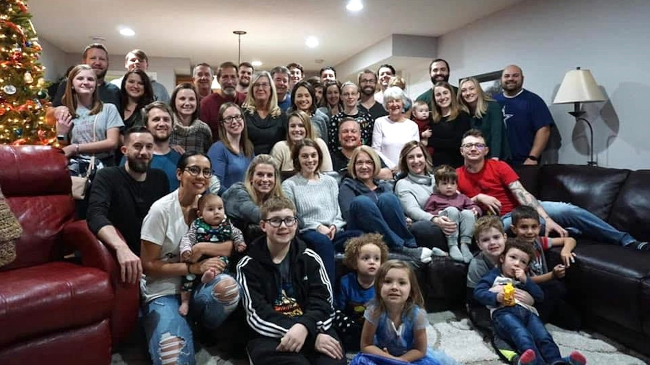 A large family gathered together in the living room with a Christmas tree in the corner