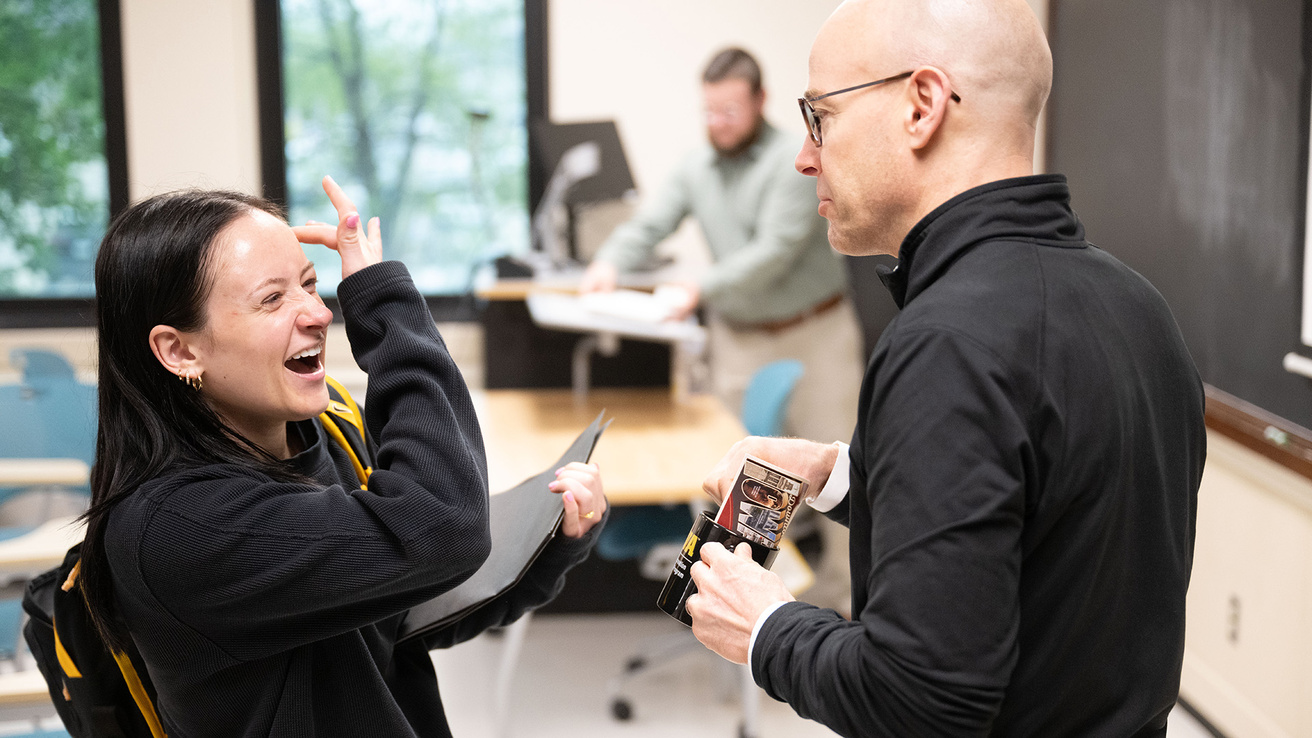 a student athlete speaks with a professor in a classroom