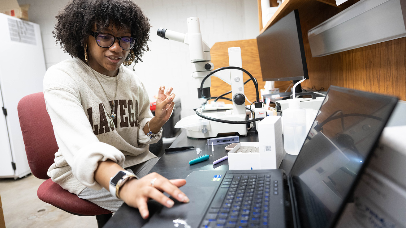 a woman reaches for her computer while doing work in a biology laboratory