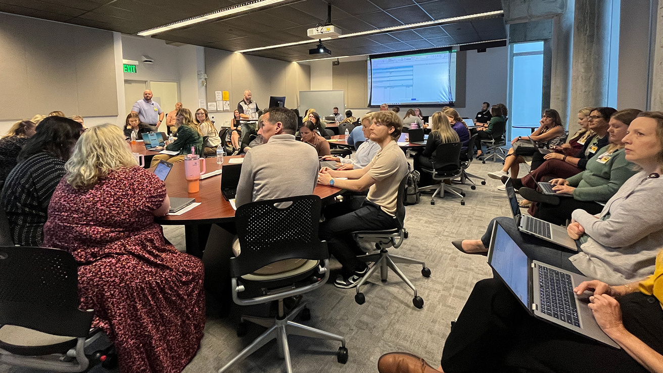 people around tables in a conference room looking at projection screens