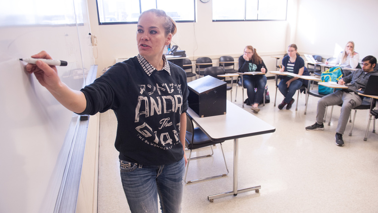 A woman writing on a whiteboard in front of a class